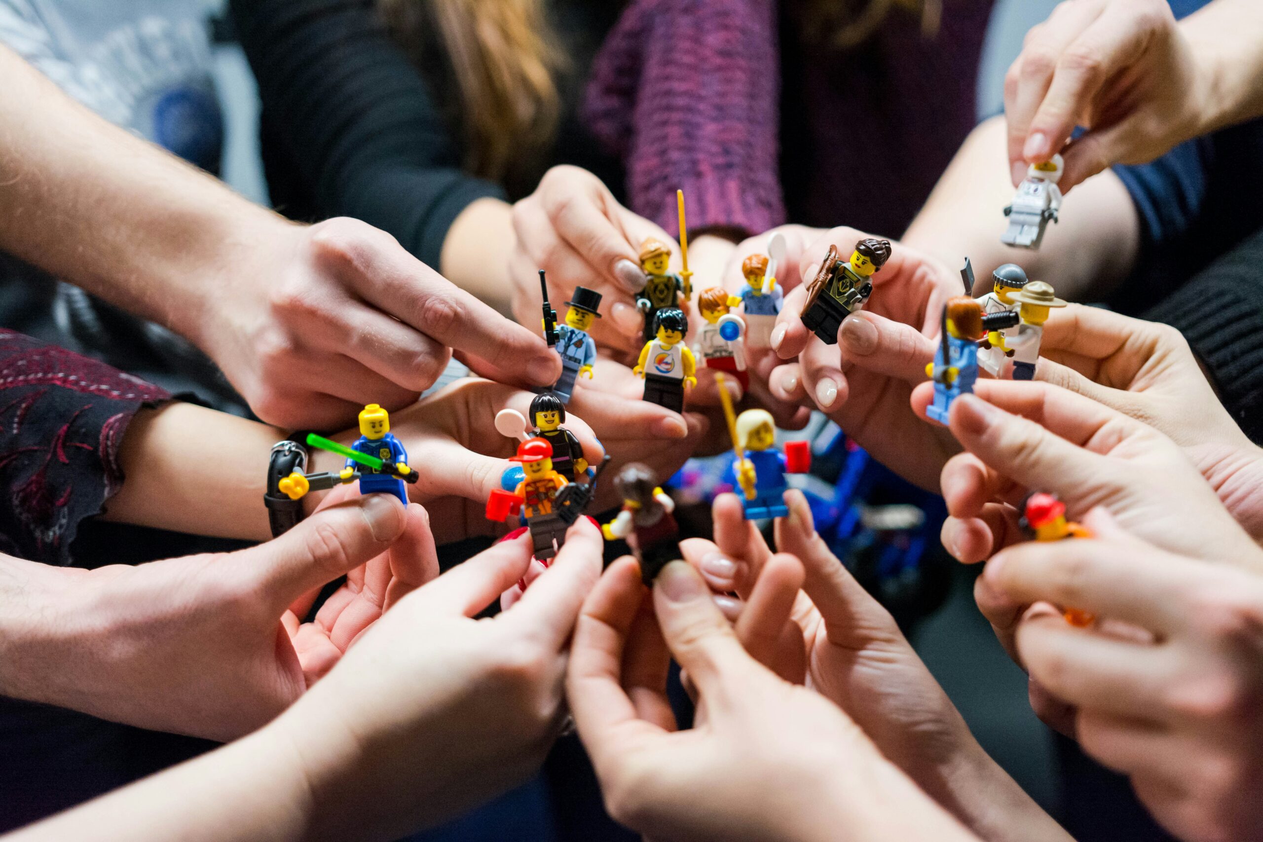 Group of people holding LEGO minifigures together in a shared hands-on play scene