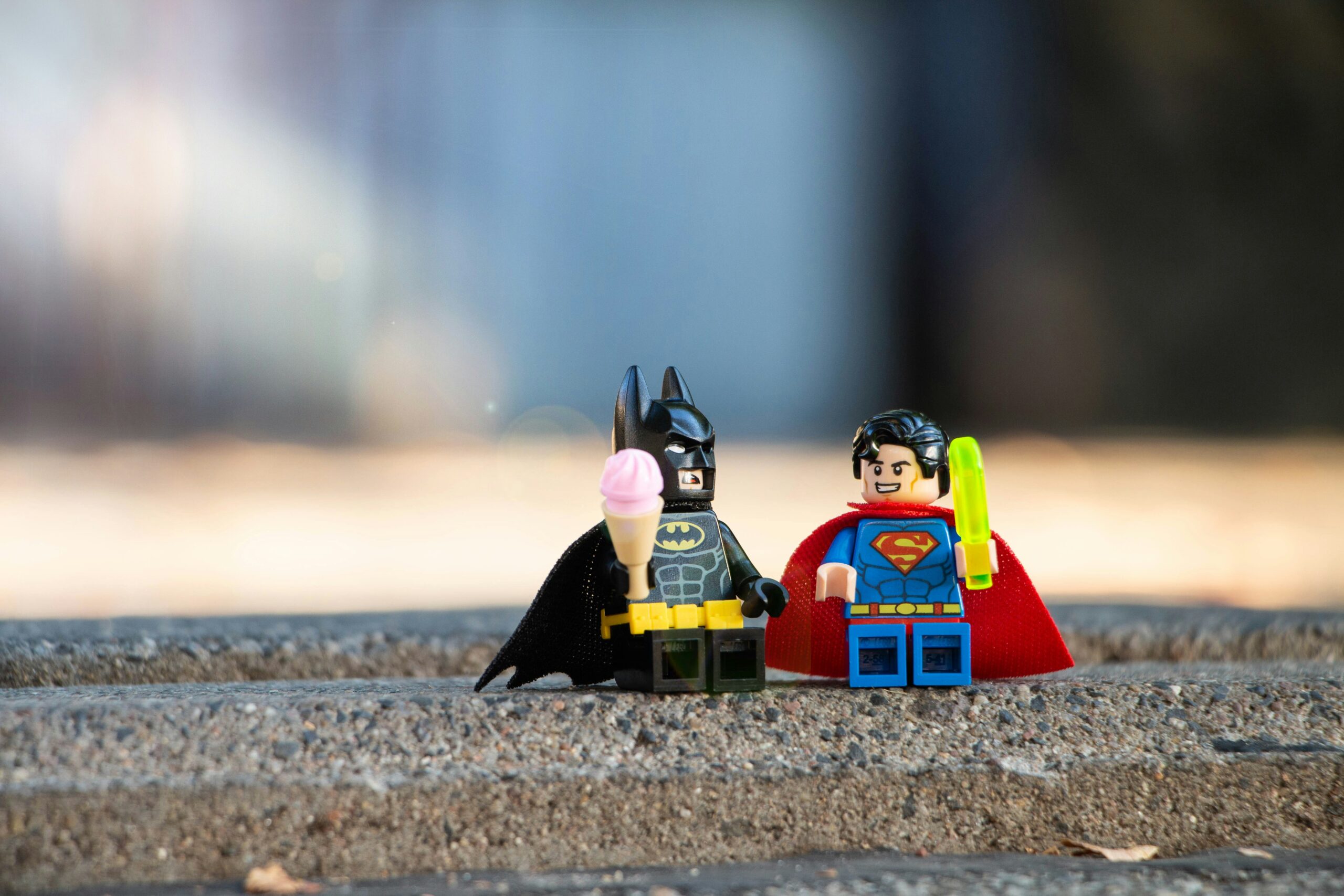 LEGO Batman and Superman minifigures sitting together on a ledge holding ice cream treats